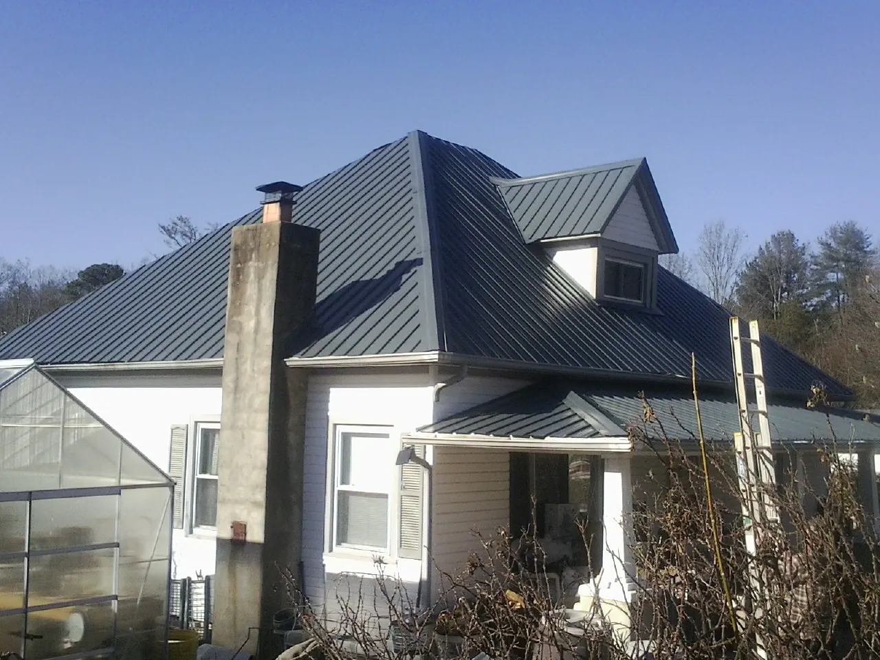 Dark blue standing seam metal roof on a white farmhouse with dormer — Slate & Tile Roof Repair by Roofing Brothers in Sharpsburg