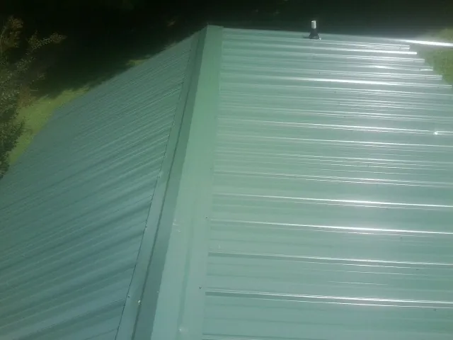 New green metal panels meeting at the ridge of a roof — Flat Roof Repair work by our crew in Sharpsburg