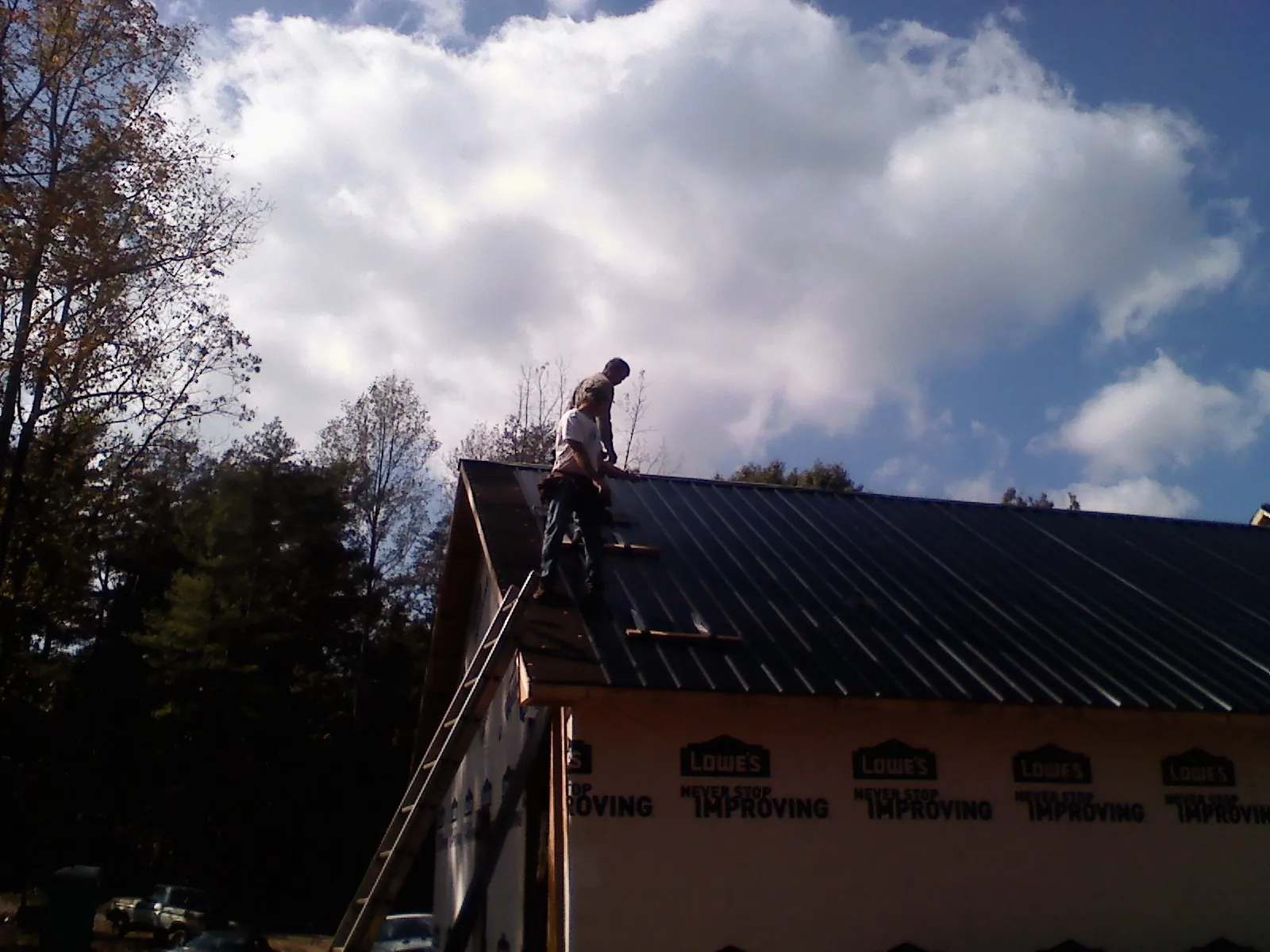 Roofer fastening dark metal panels high against a cloudy sky, from a Roof Inspection job in Sharpsburg